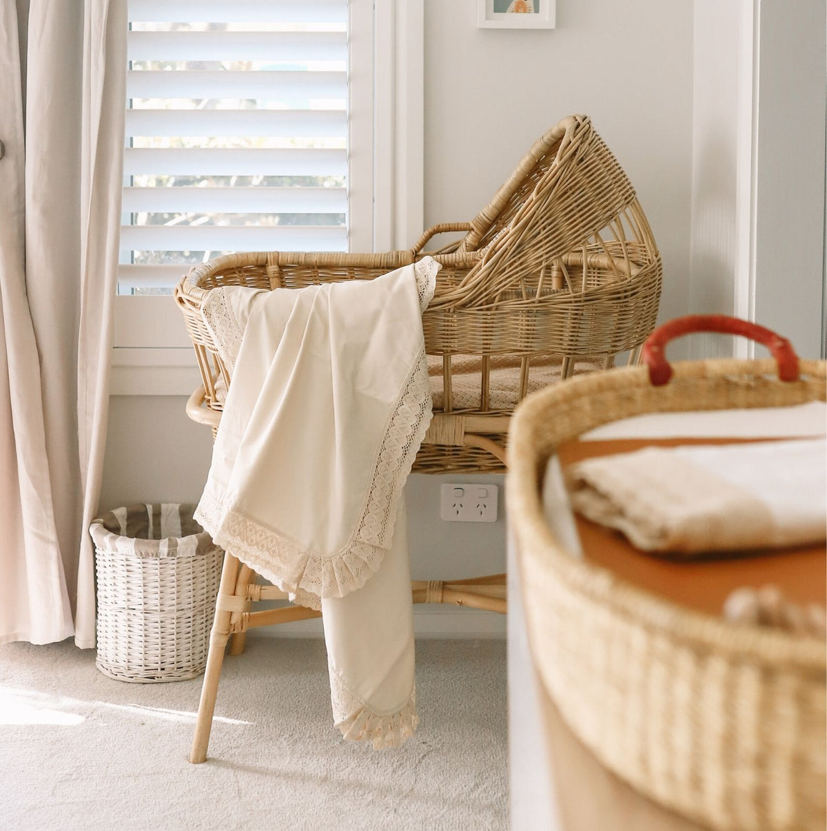 Cream coloured lace edged baby blanket hanging over a wicker vintage bassinet in baby nursery