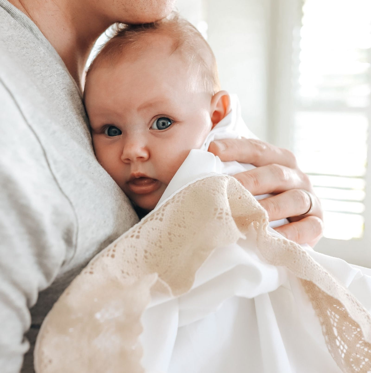 Father and baby girl wrapped in a lacey edged white blanket with cream of beige lace