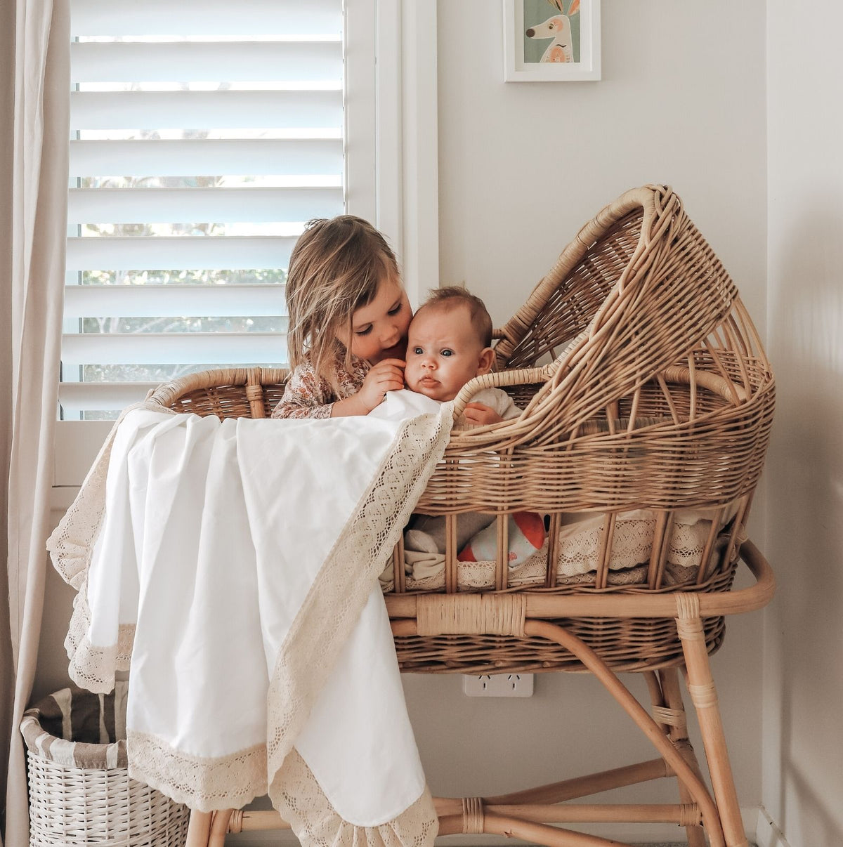 Hieloom WHite baby blanket with natural or beige lace edging hanging over a vintage cane bassinet